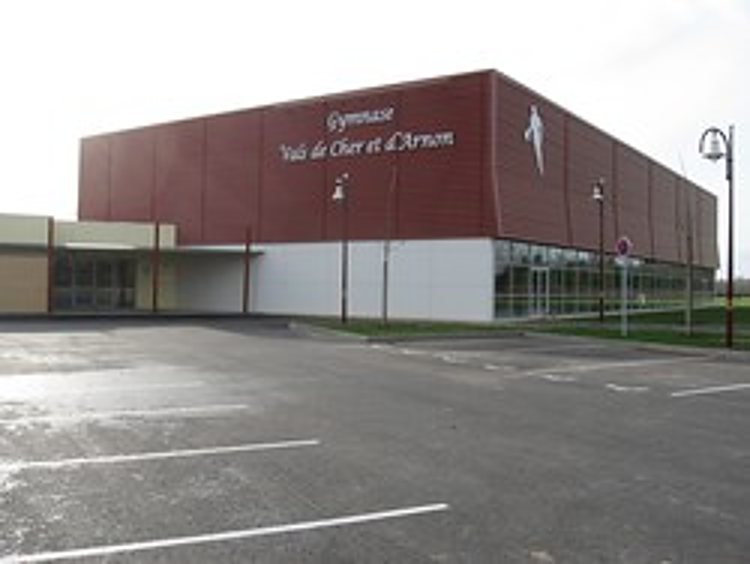 Bâtiment moderne du gymnase Val de Cher et d'Arnon avec façade rouge bordeaux, grandes baies vitrées et parking au premier plan.